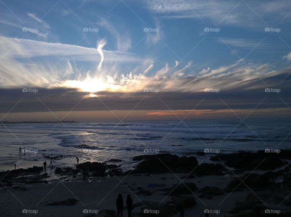 bright light illuminating the clouds above the ocean and beach on a California evening at sunset