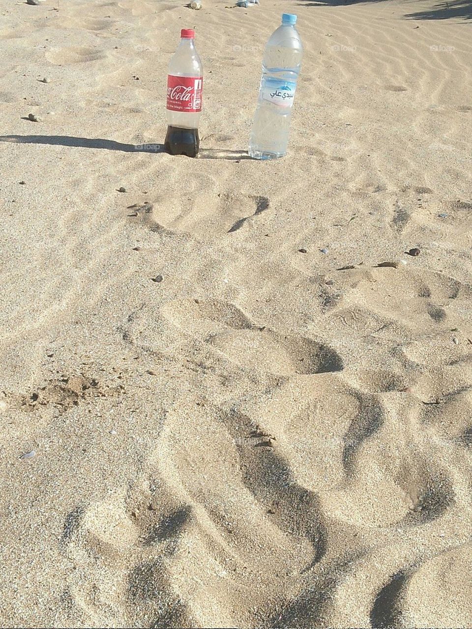 Two bottles:  cocacola and pure water on sand.