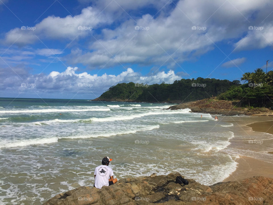 Boy listening to music looking at the sea on the beach rocks