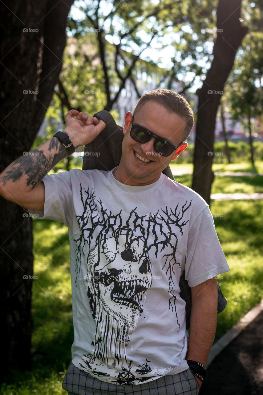 young man with tattoos walks in the summer in the park