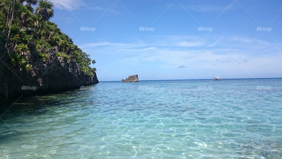 Coral mountain in Roatán Honduras. A calming travel image with soft blues and clear water in the foreground and darker blues in the sky with a few clouds.