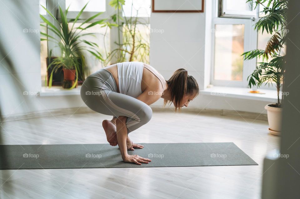 Young fit woman practice yoga doing asana in light yoga studio with green house plant