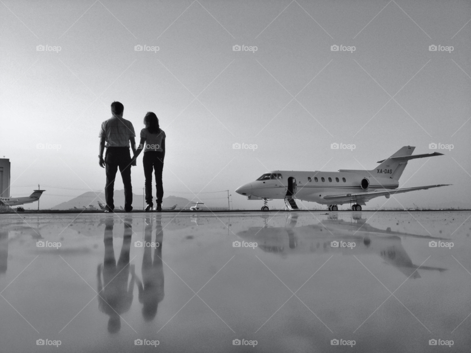 Leaving on a jet plane. Couple holding hands under hangar ready for a private jet plane