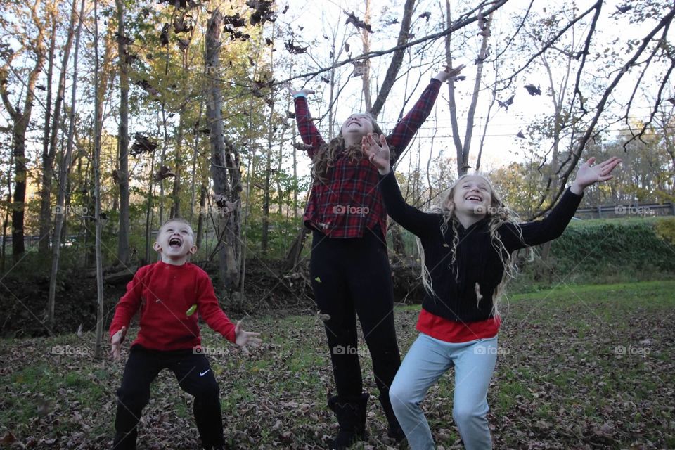 Three siblings having fun playing in the fallen leaves. 