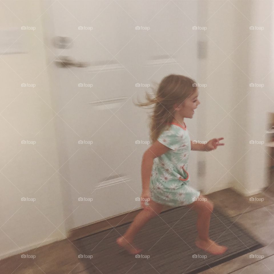 Little girl running inside the house wearing a green dress.