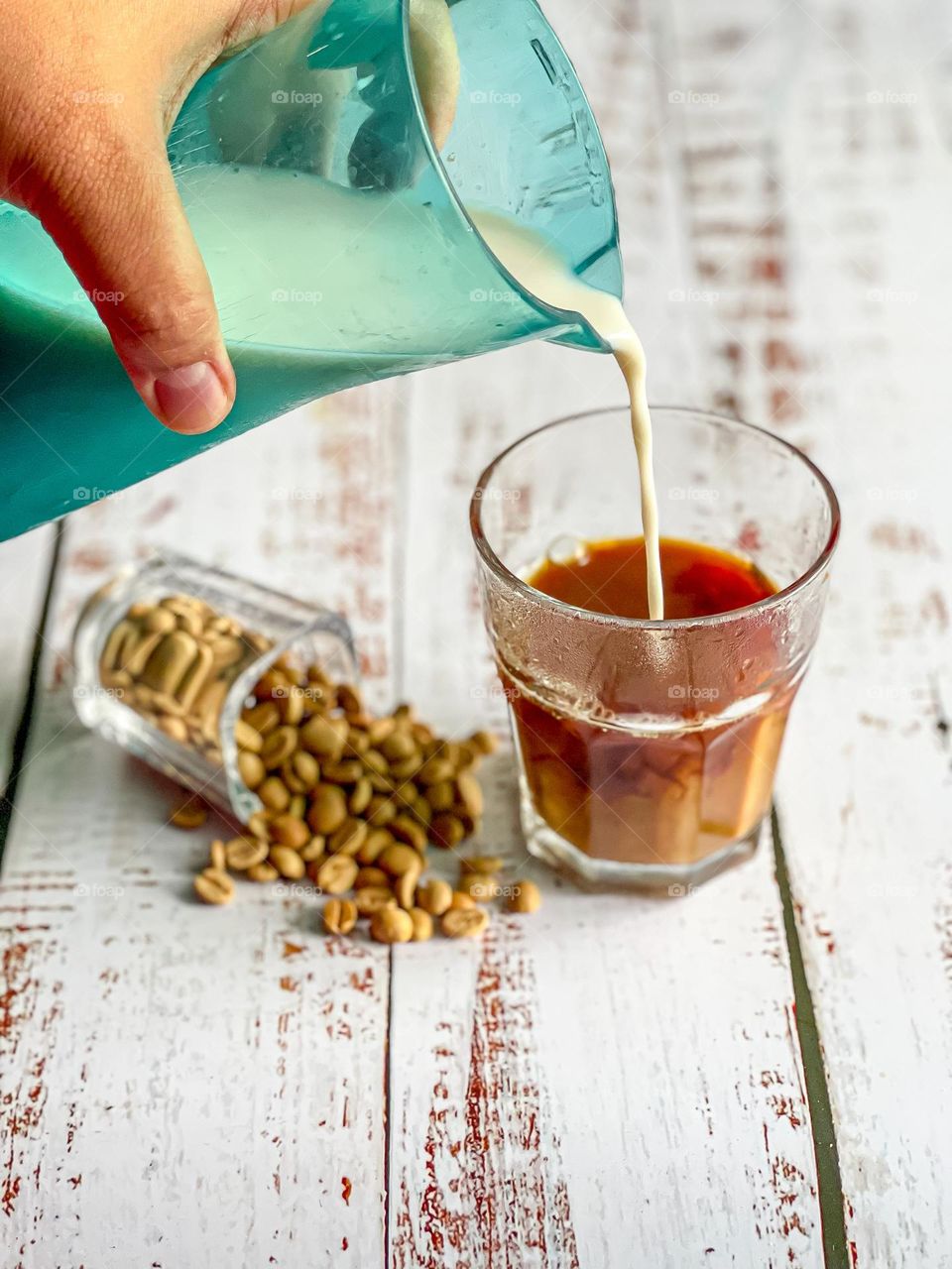 Pouring milk into a cup of coffee with spilled coffee beans on the side with bright colour