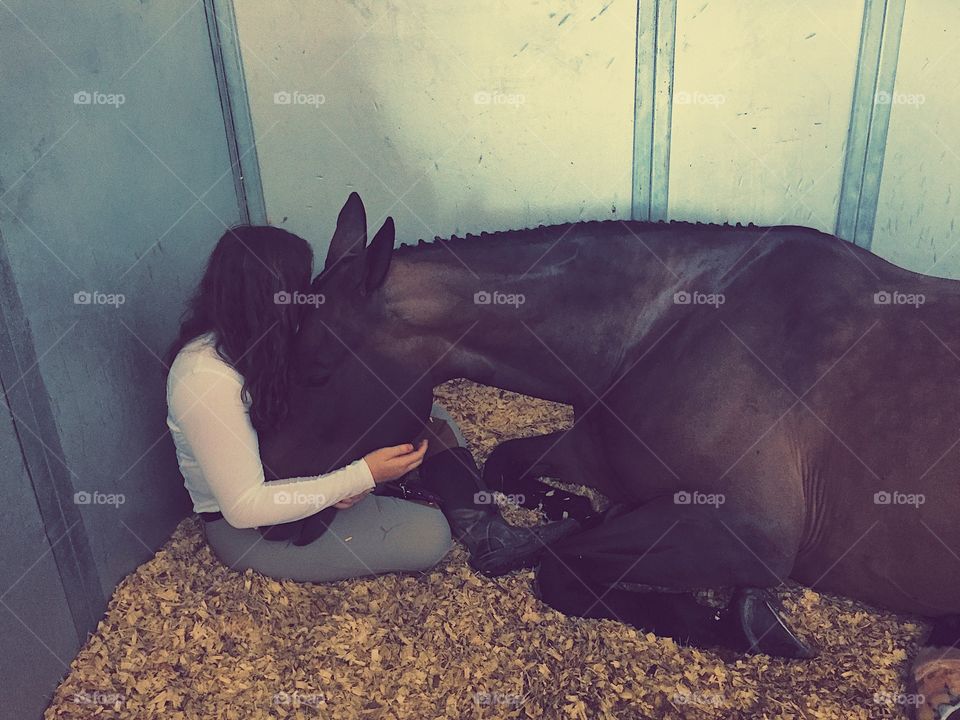 Teenage girl cuddling her horse while he falls asleep on her lap.