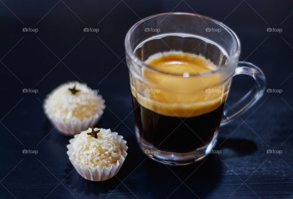 A cup of espresso coffee accompanied by two sweets of condensed milk and shredded coconut, finished with cloves.