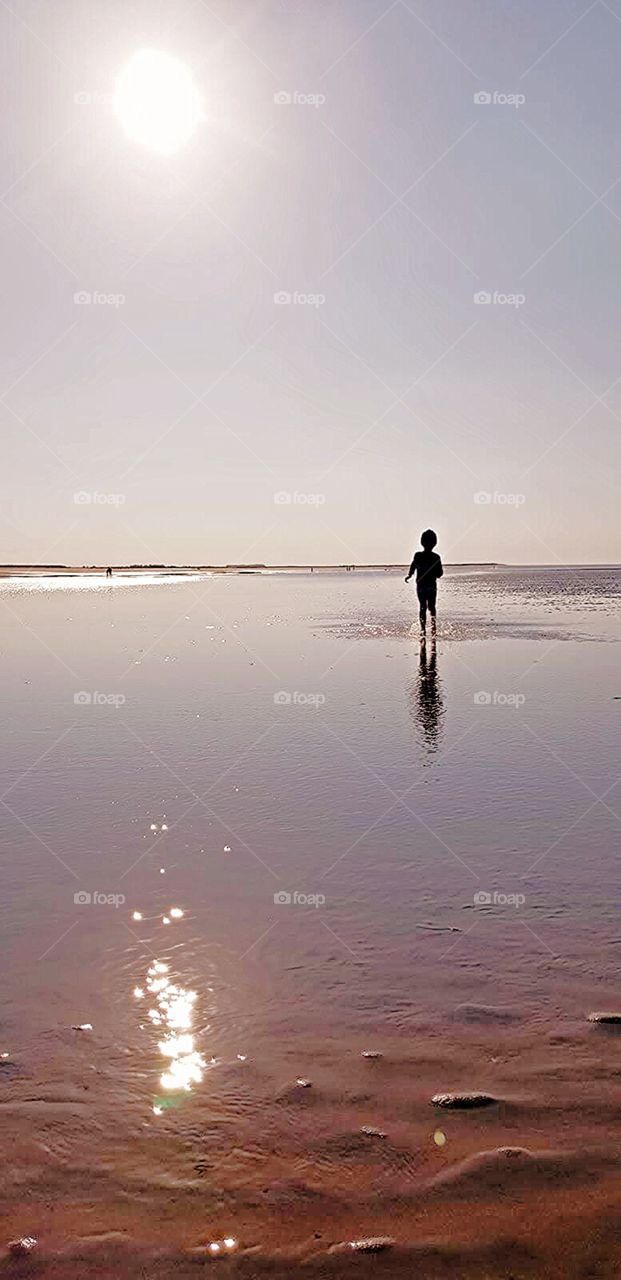 small child running on the beach seaside waves water glowing pink in the summer sun