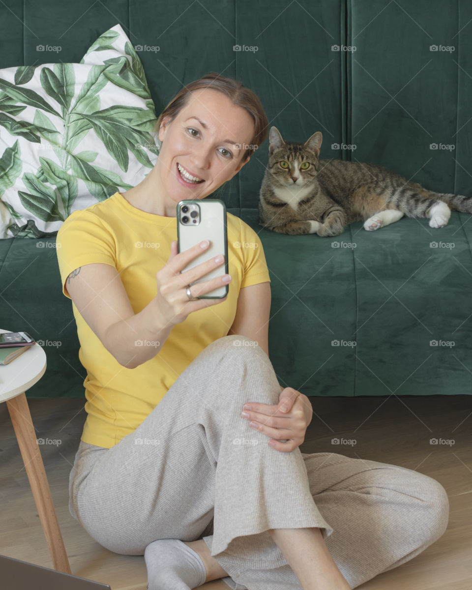 Yong Woman sitting on a floor making a photo with a cat on the couch