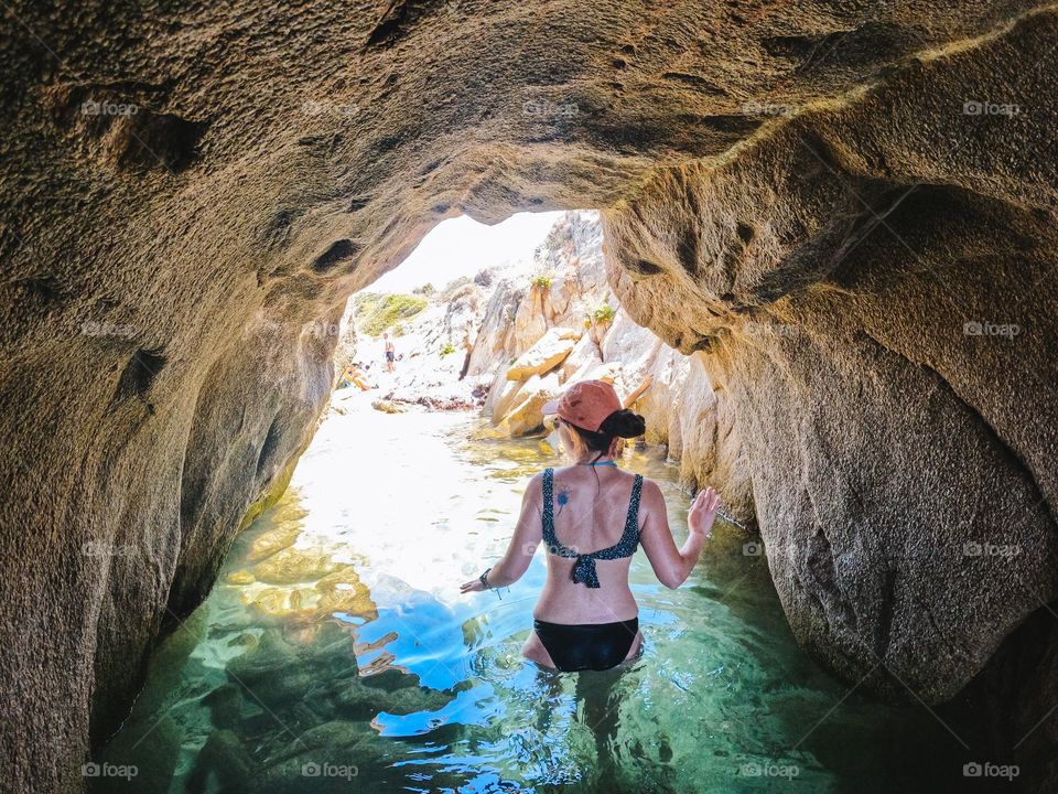 Young woman, while in vacation, exploring a cave at the beach with crystal clear water.