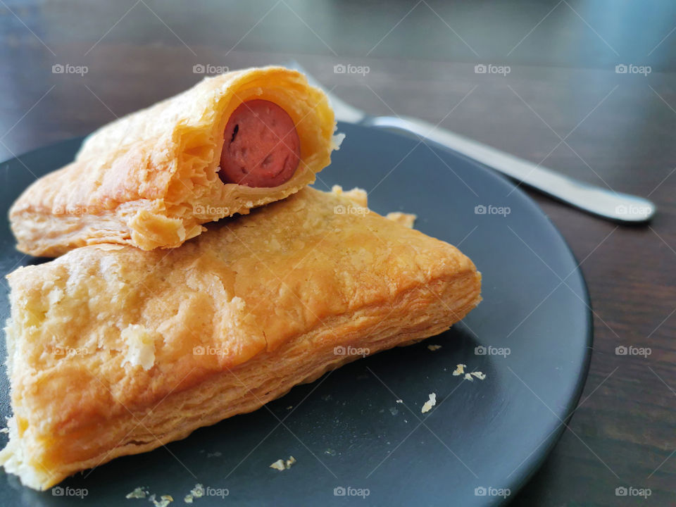 Sausage roll with hot dog in a black blue plate on wood brown table.