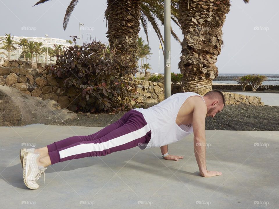 hombre haciendo flexiones en la calle ejercitándose con vistas al mar