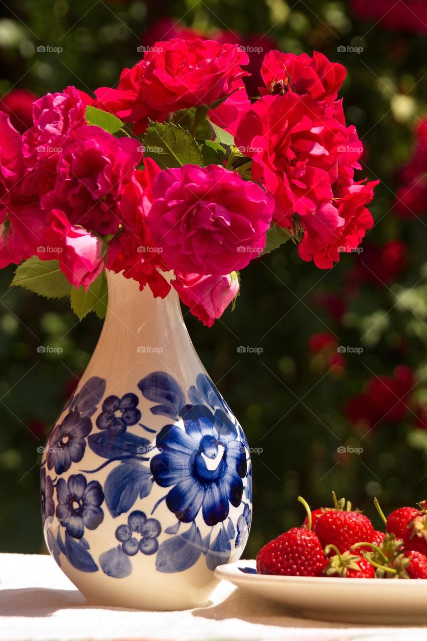 Vase with roses and plate with strawberries