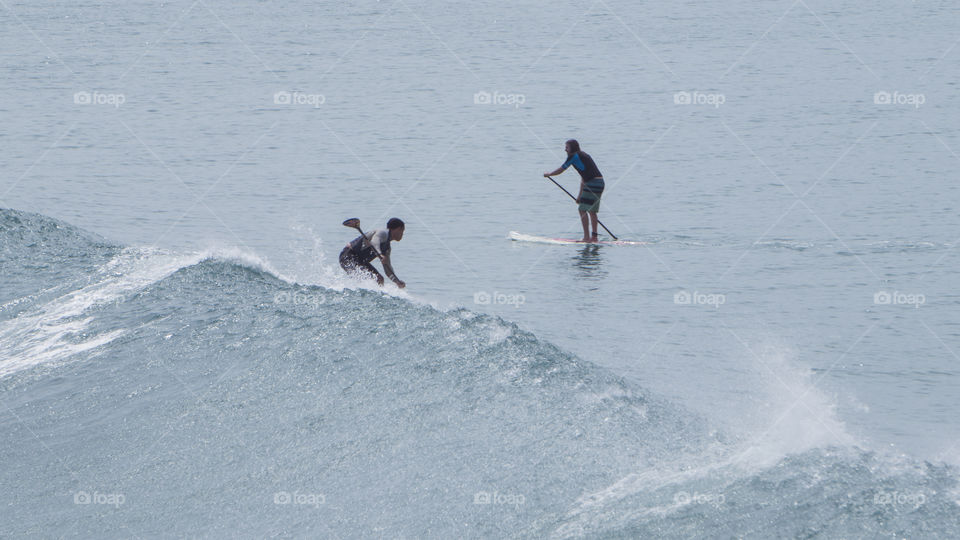 Two men go surfing and paddle boarding in the ocean during summer