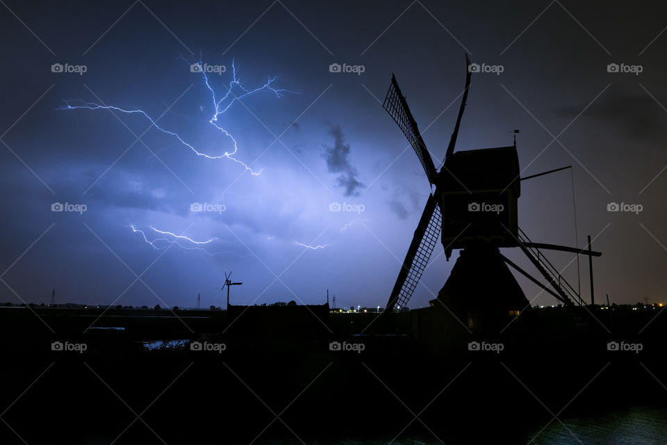 A dutch windmill is silhouetted against the sky with lightning. Photograph was taken near the city of Leiden, Netherlands.