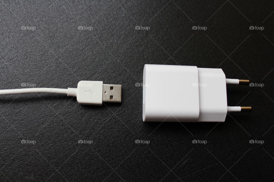 White USB cable and charger separated on a black texture background