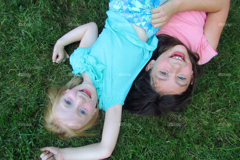 Two young girls laying on the grass together 