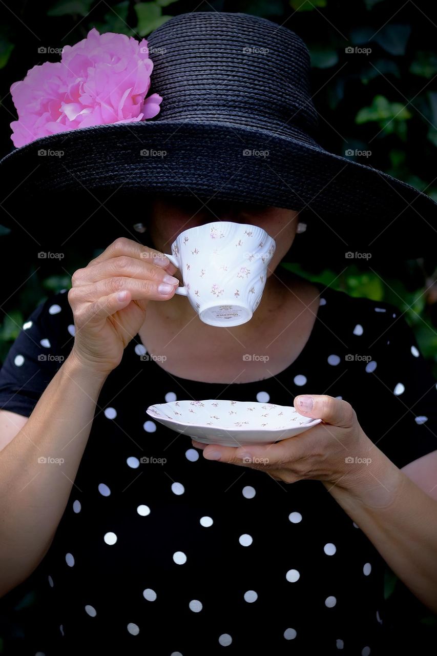 Close-up portrait of woman with black hat sipping tea from a porcelain cup. 