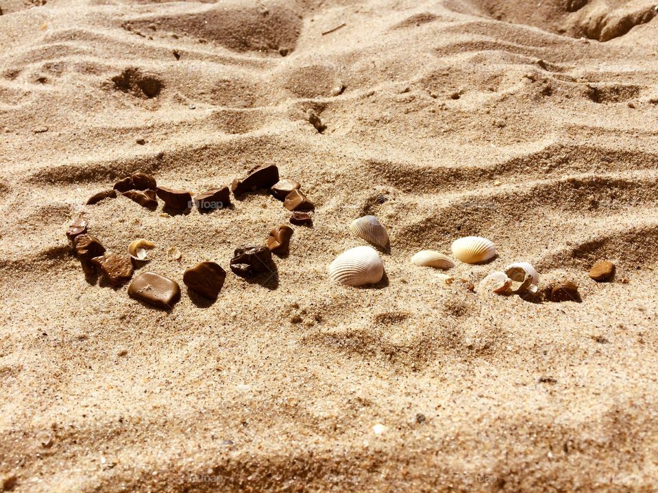 Love heart made with stones and shells on a sand