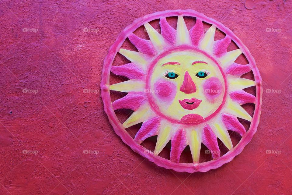 A Mexican reddish pink sun face isolated on a similar colored wall.
