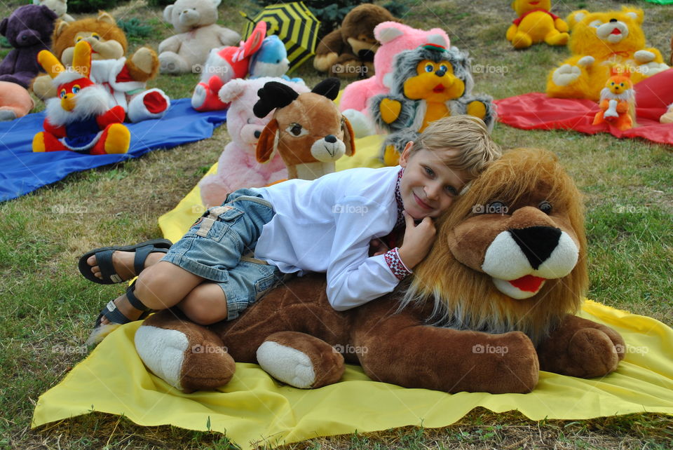 Cute boy lying on a toy lion in the summer in the park among soft toys