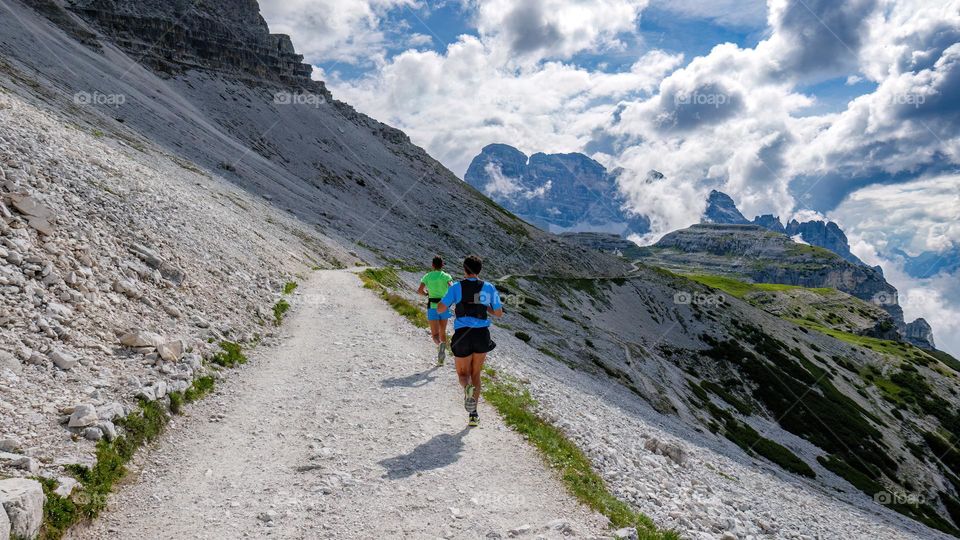 Rear view of two men running on gravel path in magnificent mountains