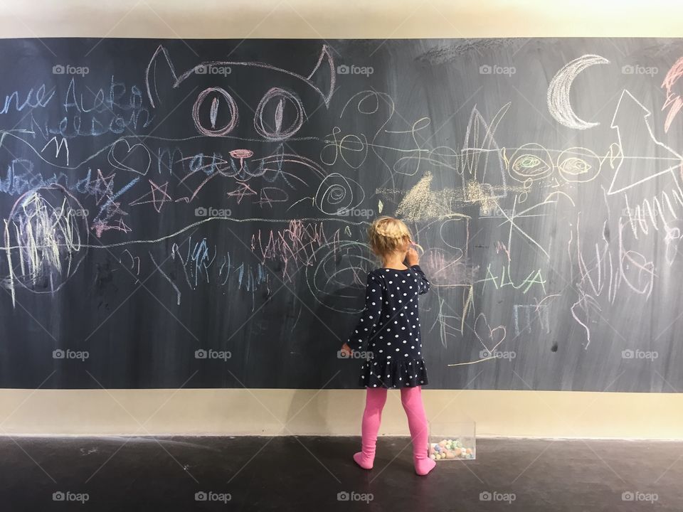 a small girl drawing with chalk on a blackboard in a playroom at a shopping center in Malmö, Sweden.