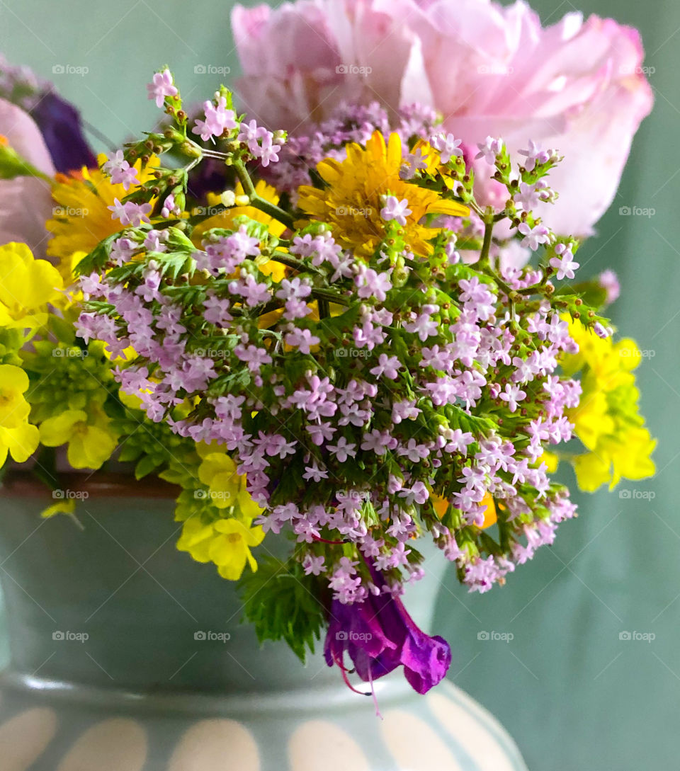 Wildflowers in pinks, yellows & orange, placed in a green vase with pale green background 