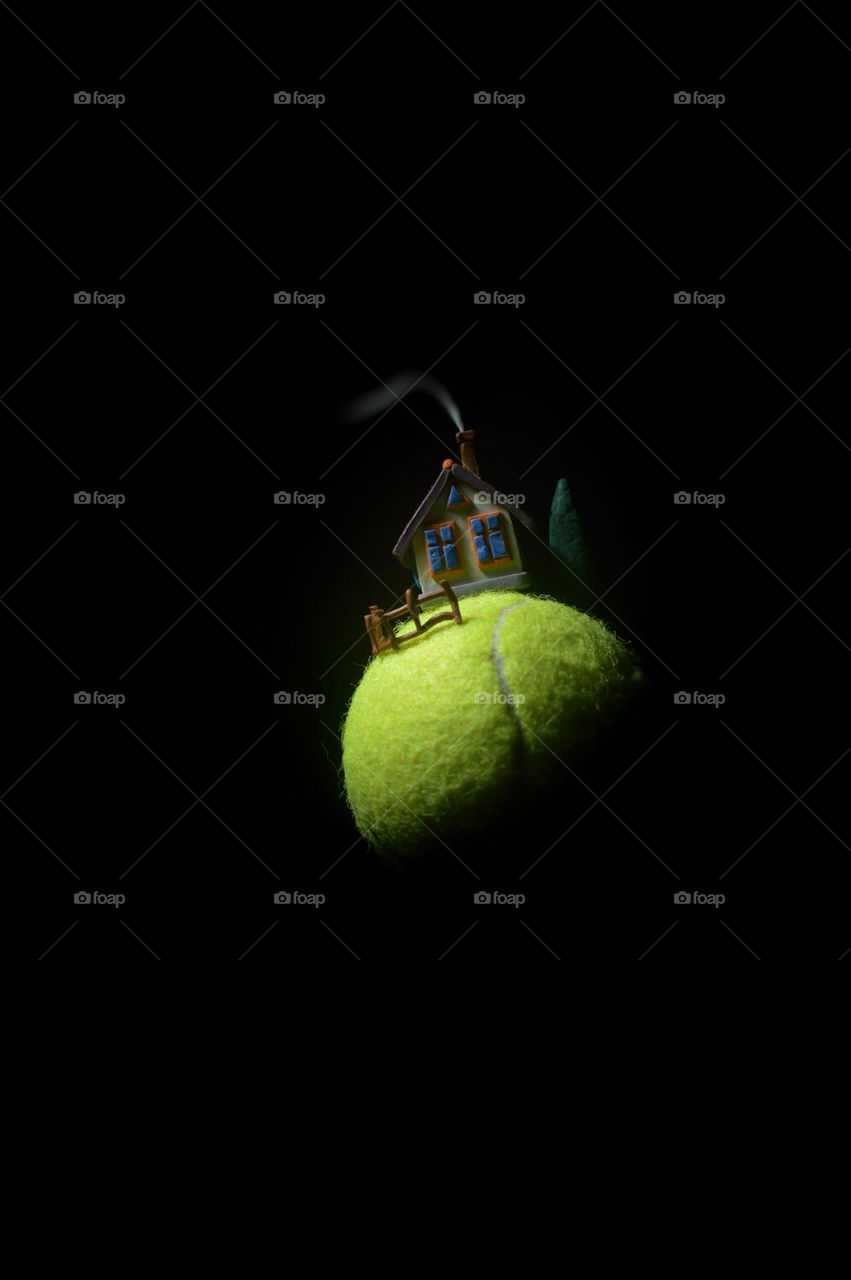 volumetric plasticine miniature. small planet tennis ball. there is a plasticine house on the ball. a one-story house with smoke from a chimney in complete darkness. a small fence and a tree.