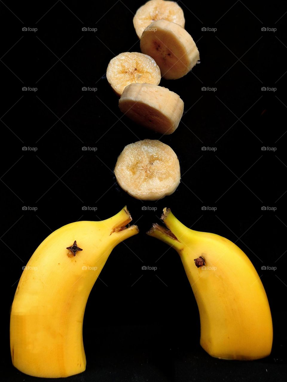 Yellow color. Edible still life. Two parts of yellow bananas in the form of dolphins with open mouths look at mugs of cut bananas that fall from above. Background black