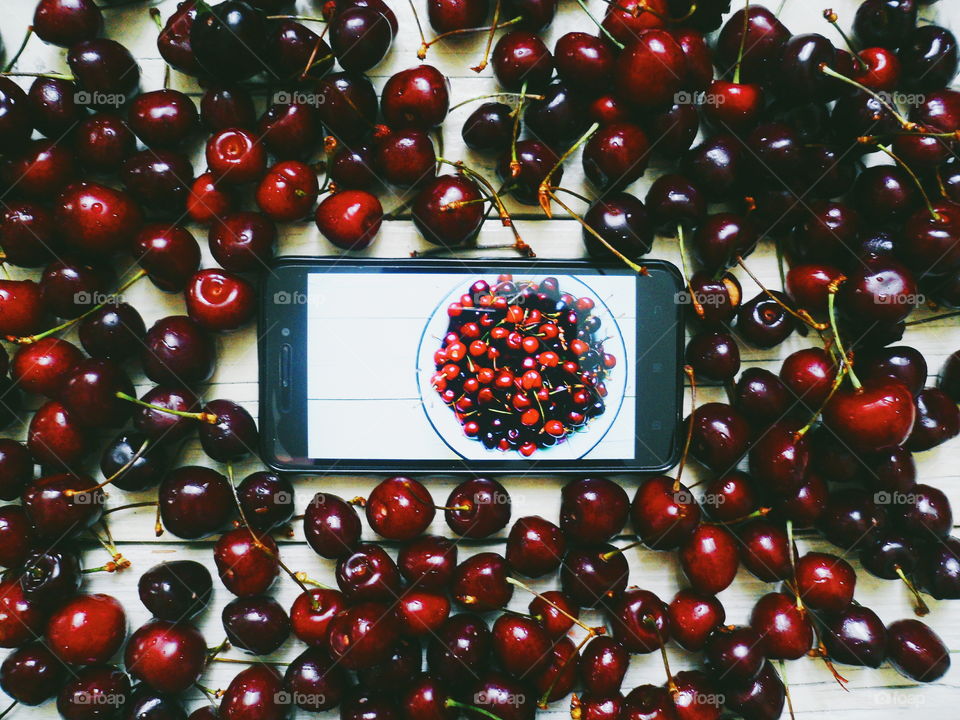 cherries on white background and smartphone with photo