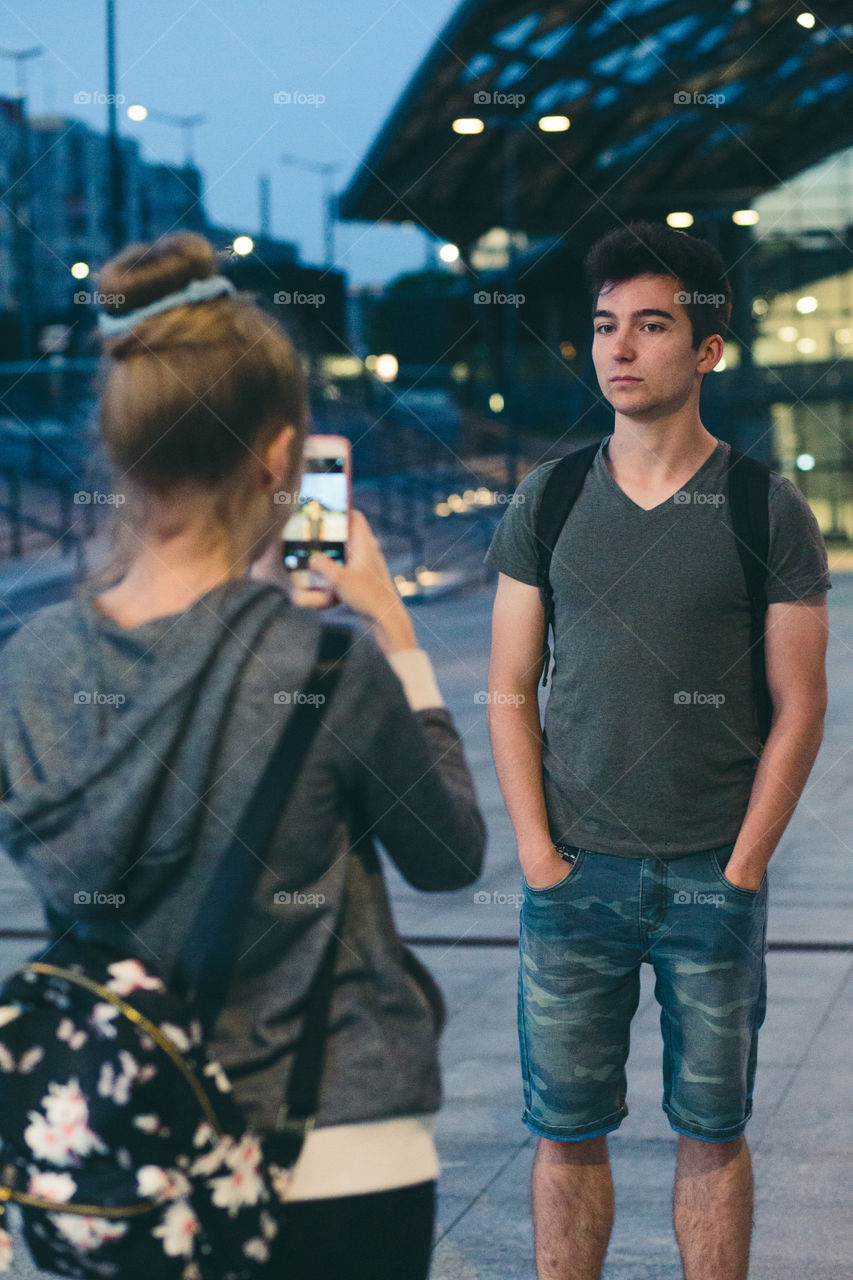 Young woman taking photos her friend, using a smartphone in the city at night