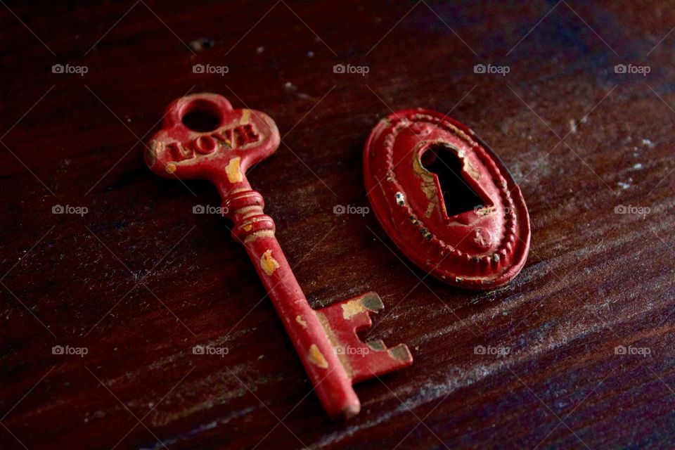 Red rustic vintage key with the word “LOVE” and keyhole on dark wooden surface