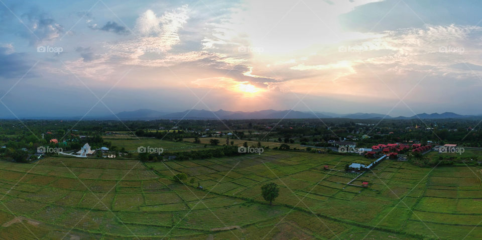 Beautiful Panoramic aerial view of village in the countryside farming area of Chiang Mai, Thailand with rice fields, houses, buddhist temple, forest and mountain during the evening sunset.