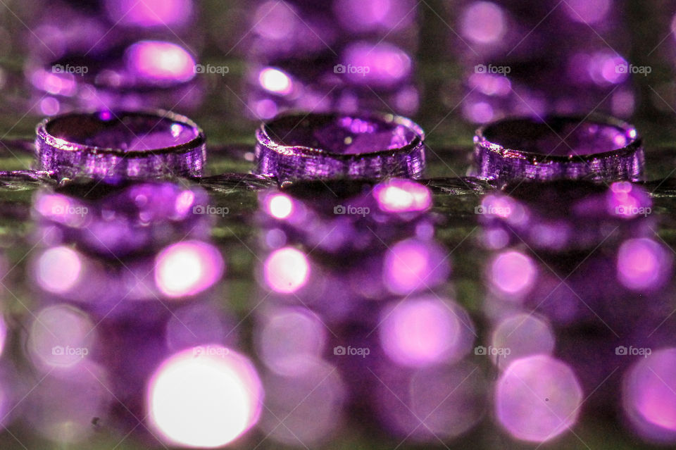 A macro shot of some gemstone net mesh. Three gems are in focus in the foreground with light reflected in front & behind the gems creating circles of reflected purple light rising in the background. 💎