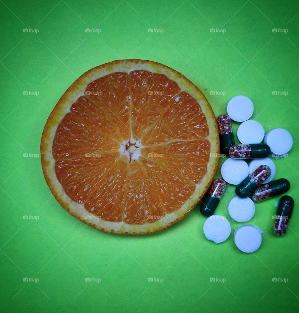 Vitamins natural and in medicinal forms.  A sliced ​​orange lies on a green background.  Next to the orange are vitamins in capsules and white tablets.  Selection for natural fruit