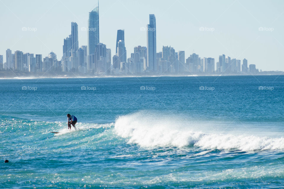 Surfer surfing on sea with city skyline in background