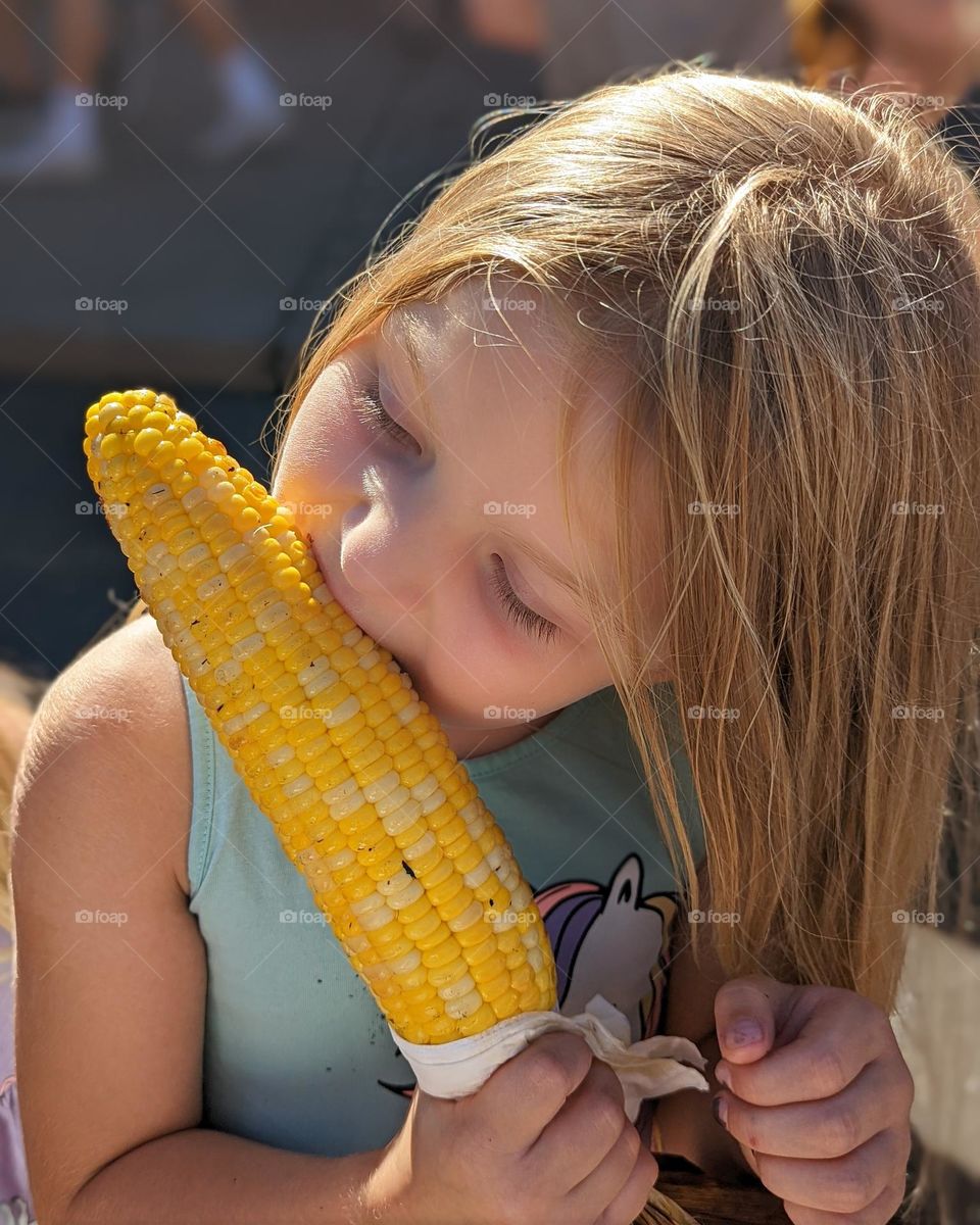 grilled corn on the cob being enjoyed by a kid on a hot spring day bright yellow corn on the cob bright blue dress