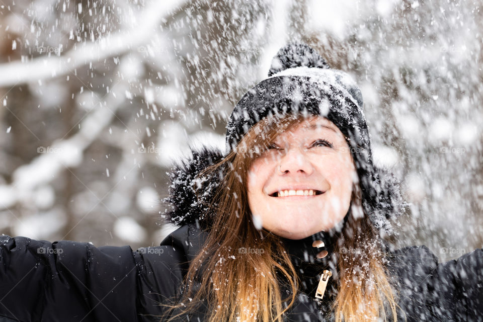 Young attractive female smiling and having fun outside in snow covered winter wonderland scene - snow falling 