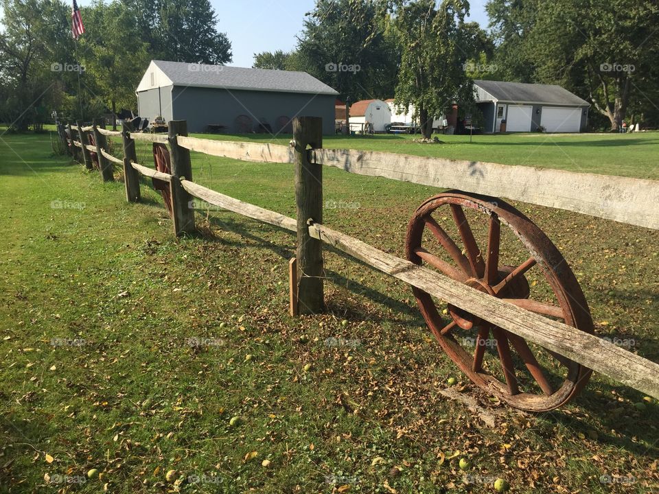 Wood fence with wagon wheel and barn and farmhouse.