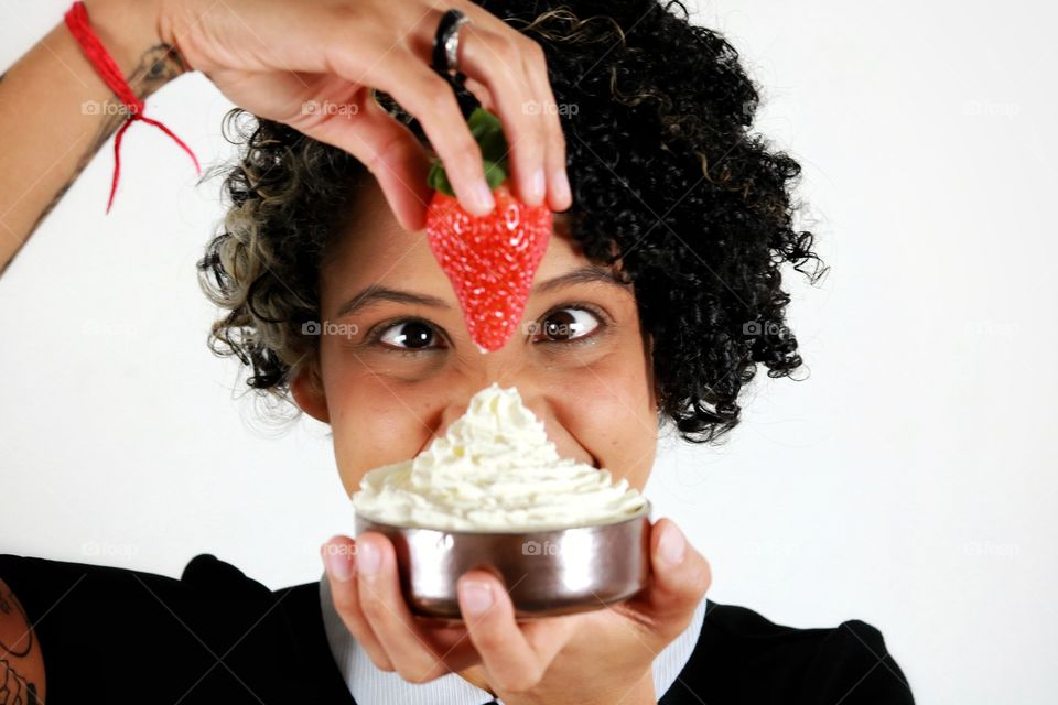 A woman eating a strawberry with Chantilly cream