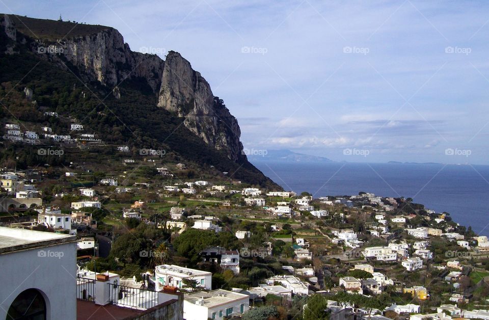 Island of Capri with its giant cliffs and white buildings spotting the hill and the distant mountains beyond