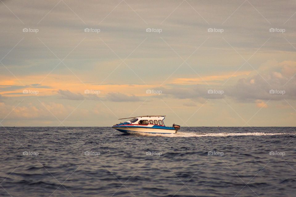 Small boat shipping in middle sea at sunset
