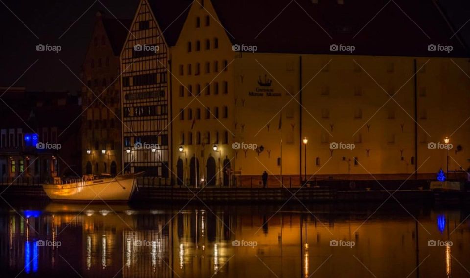 This is a night photo of a building with its reflection in the water. The building is lit up and has many windows