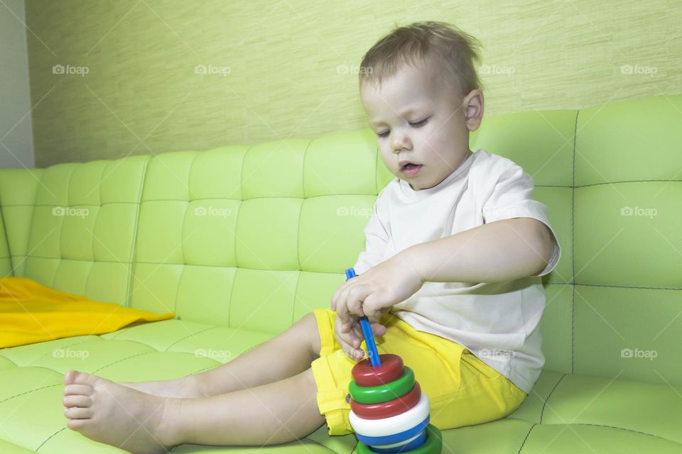 The child is having fun playing a bright pyramid educational toy, sitting on a green sofa.