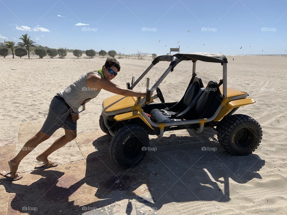 Woman pushing mini buggy in the sand because it doesn’t have reverse gear . This is a Brazil trip. 