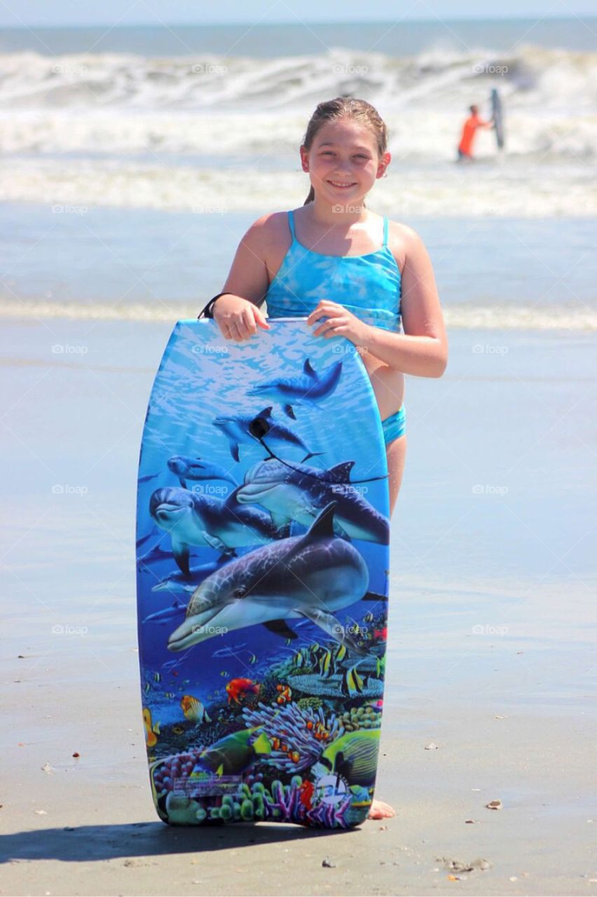 Girl standing on beach holding surfboard
