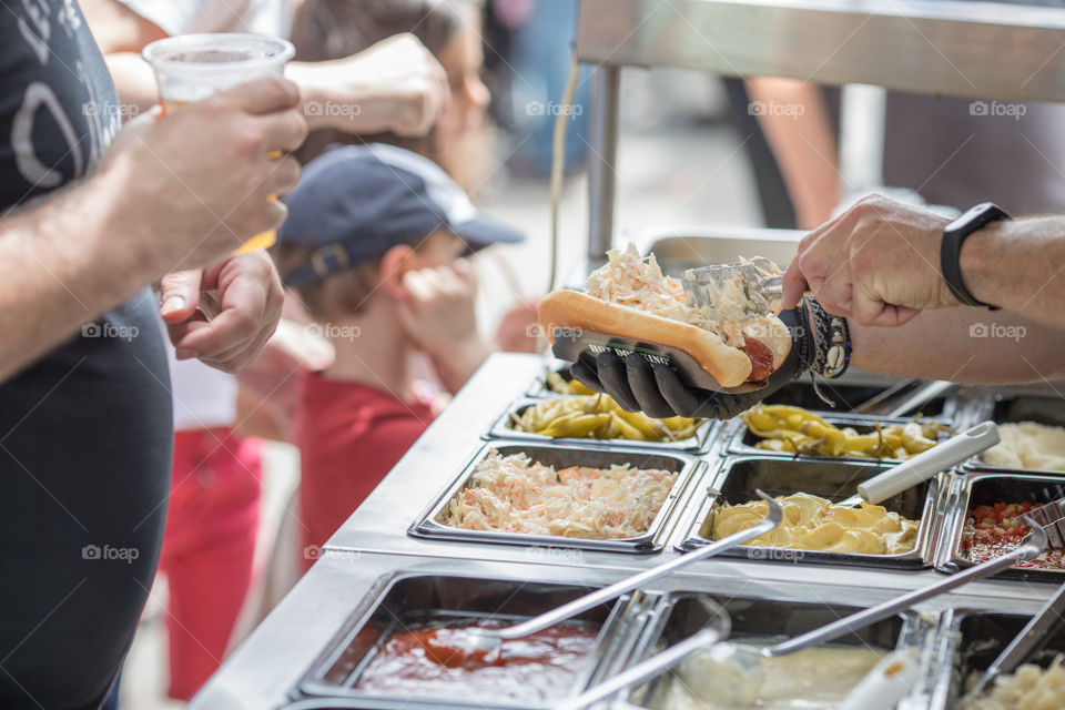 Chef's hands preparing hot dog on an outdoor fast food restaurant in front of customers.