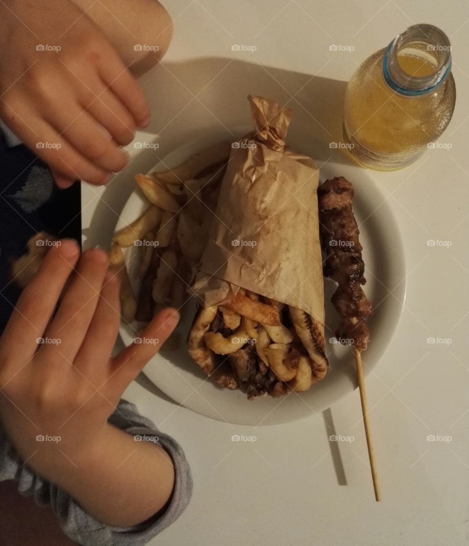 child eating pita gyros, french fries, meat stick and drinking soft drink